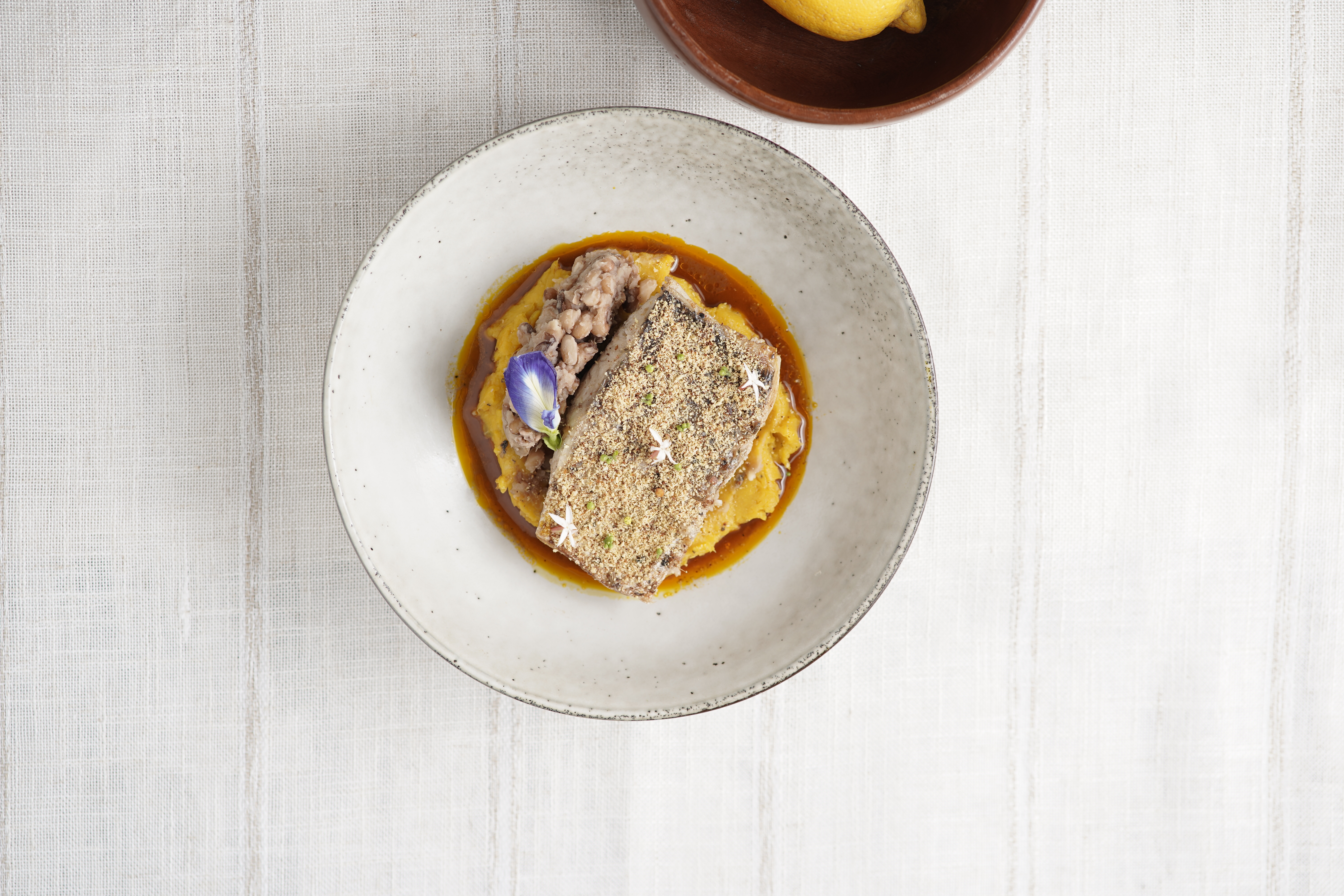 MAIN COURSE: Onunu nestled in a moqueca-inspired stew, with smashed beans on the side and pan-seared snapper coated in a crayfish–yaji–garri crust.